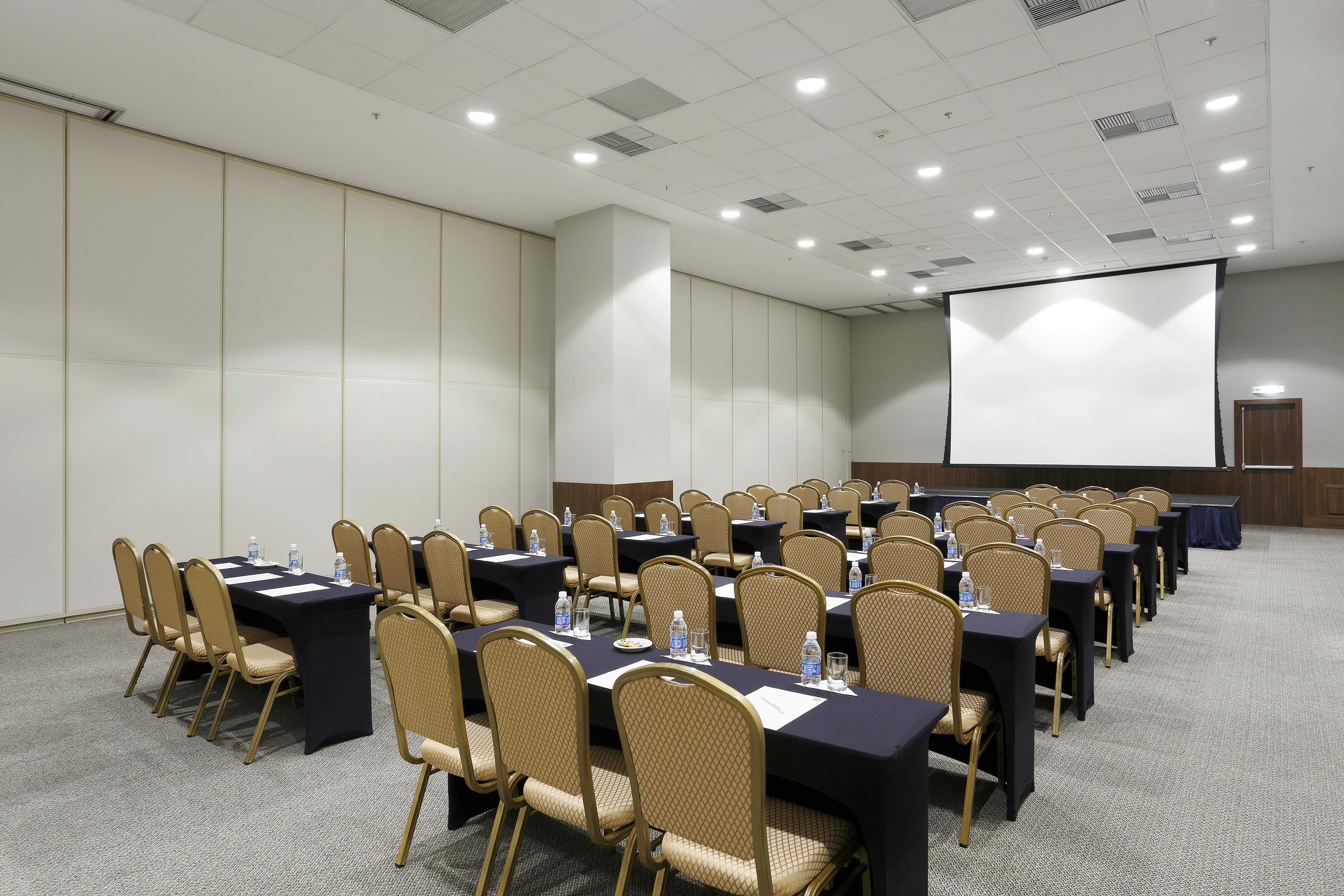 马拉蓬迪温莎酒店 里约热内卢 外观 照片 The photo shows a conference or meeting room arranged with several rows of tables and chairs. The tables are covered with dark tablecloths and have water bottles placed on them. The room is bright and spacious, featuring a large projection screen on 